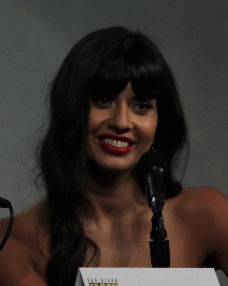 Jameela Jamil sitzt lächelnd vor einem Mikrofon bei einem Panel zur Serie The Good Place, Aufnahme 2018.